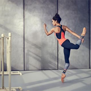  Woman stretching while standing on one leg balancing on toes in grey room 